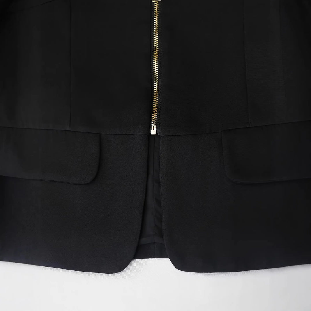 Black blazer hem and center zipper close-up with side welt pockets.