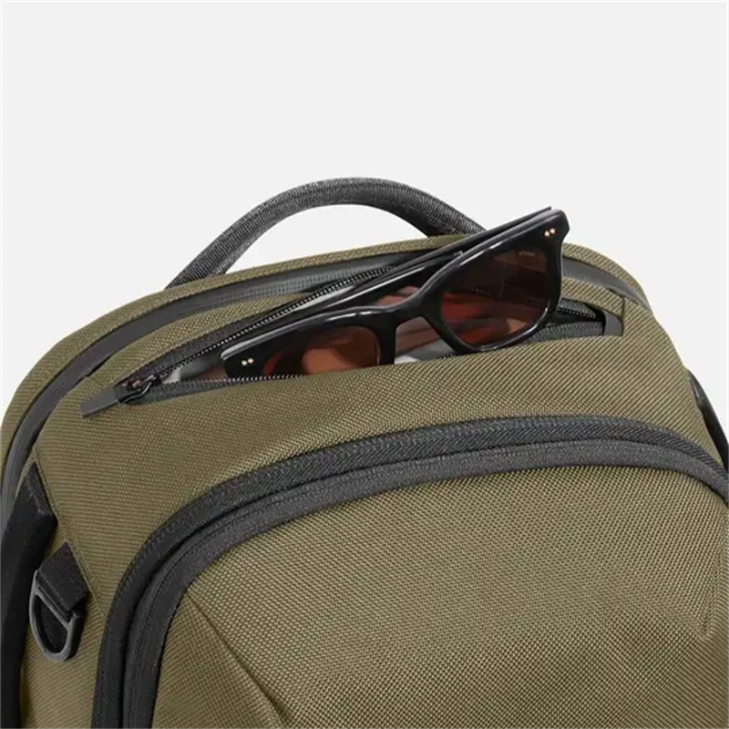 Olive green backpack top front pocket with sunglasses resting inside