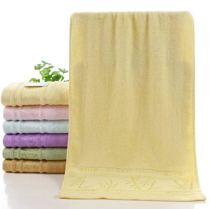 Bamboo towel set in pale cream with subtle embossed border; stacked pastel towels behind.