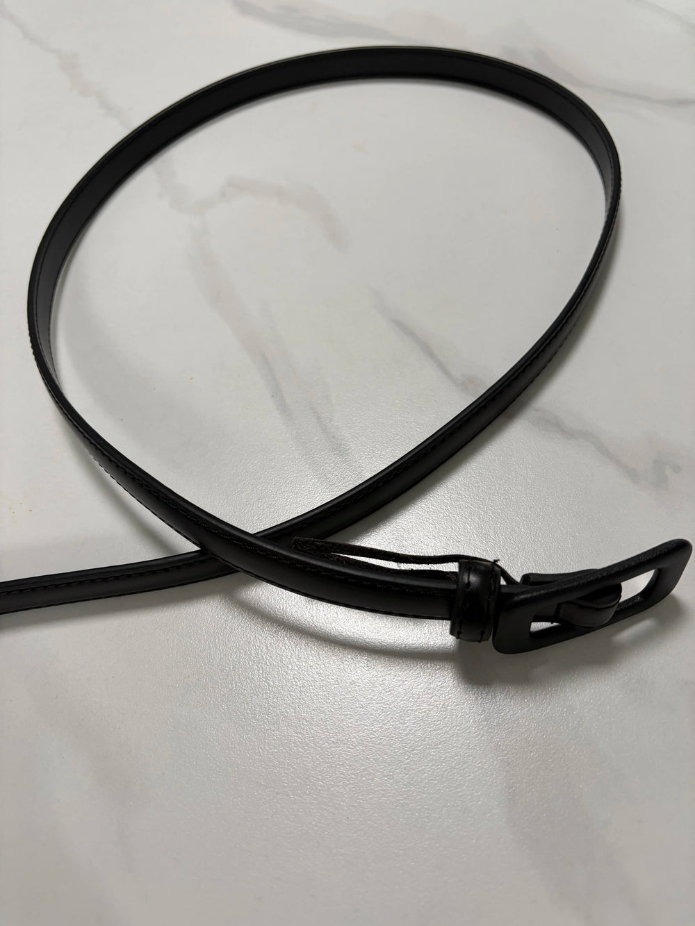Black narrow leather belt with buckle and loop, flat end visible