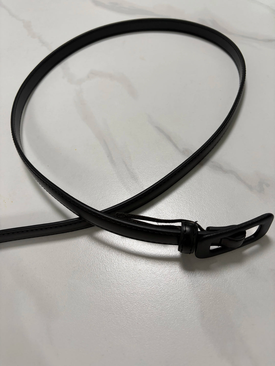 Black narrow leather belt with buckle and loop, flat end visible