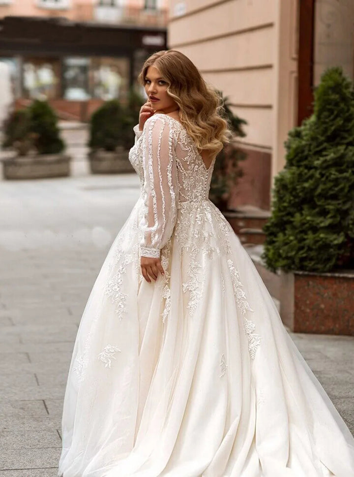 Ivory plus size wedding gown with lace appliques, sheer sleeves, and flowing tulle skirt