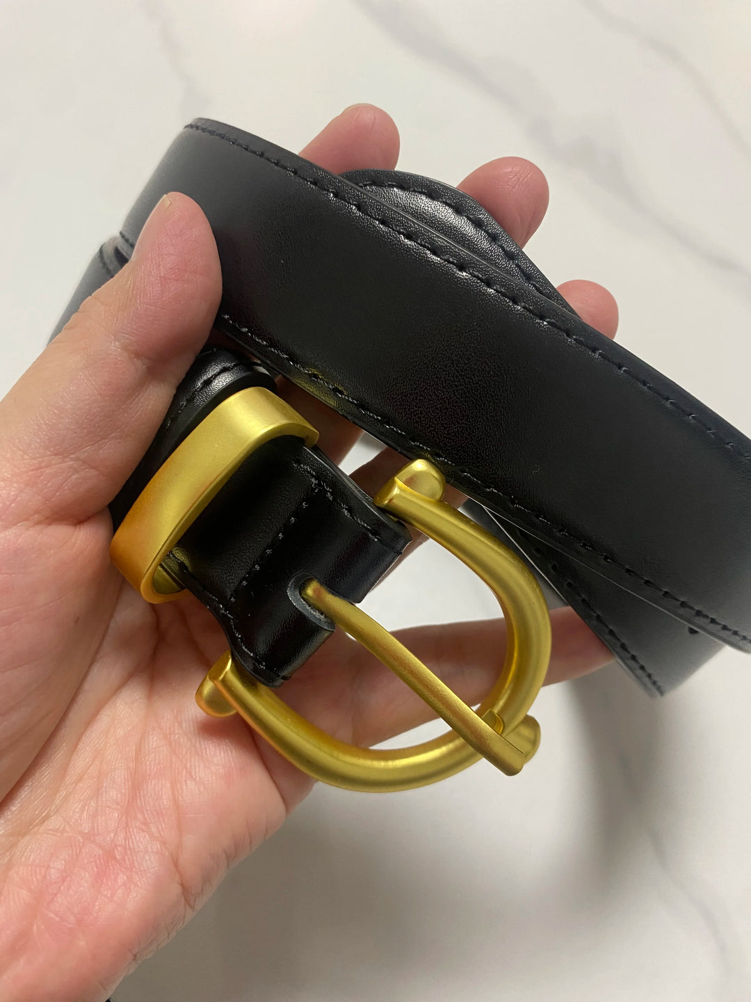 Black leather belt detail: gold-tone buckle with round bar and stitched edge