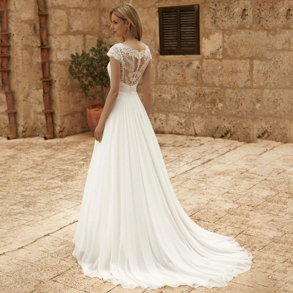Ivory lace cap-sleeve bridal gown with fitted waist and flowing chiffon skirt, rear angle