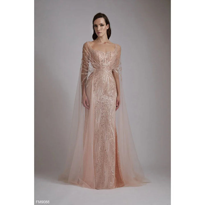 Woman wearing a sparkling evening gown with a cape against a neutral background