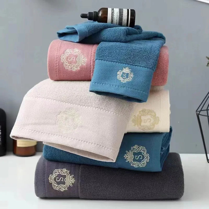 Cotton towels stacked in blue, cream, and pink with embroidered crest emblem