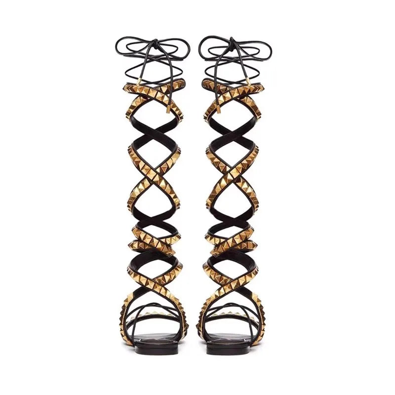 Black flat gladiator sandals with crisscross straps, gold stud trim, and lace-up ankle ties