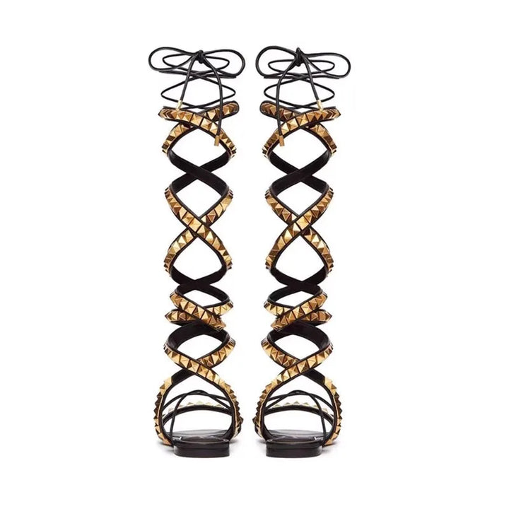 Black flat gladiator sandals with crisscross straps, gold stud trim, and lace-up ankle ties